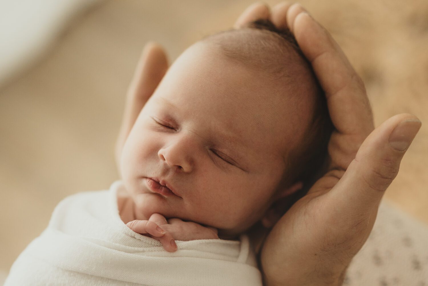 Portraitaufnahme eines Neugeborenen Baby in den Händen eines Elternteils dabei kann man ein paar Finger aus dem Wrap guckend sehen