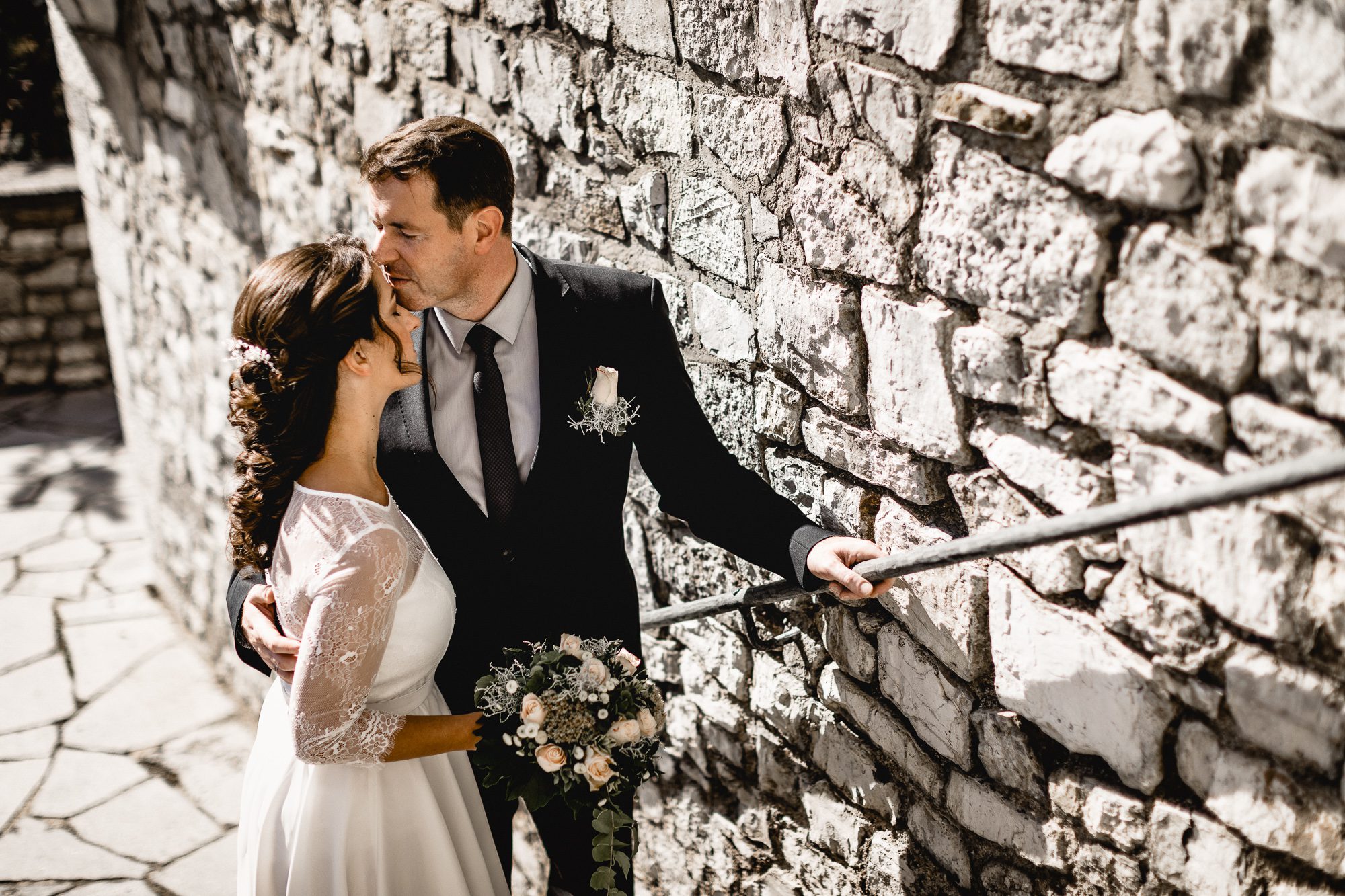 Brautpaar steht nahe einer Mauer und bräutigam küsst seine Braut