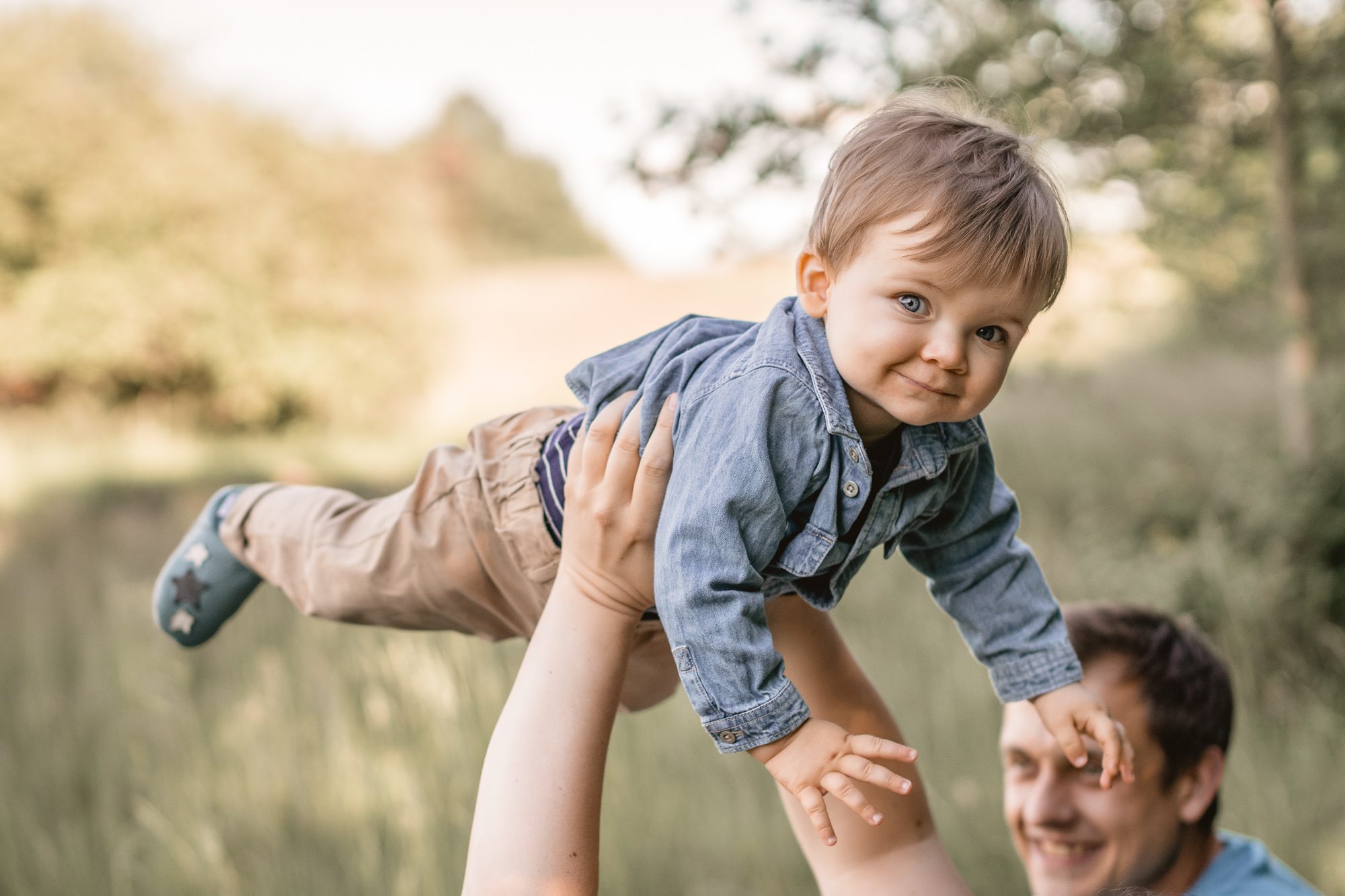 Babie welches hoch in die Luft gehalten wird und für ein Foto in die Kamera lächelt