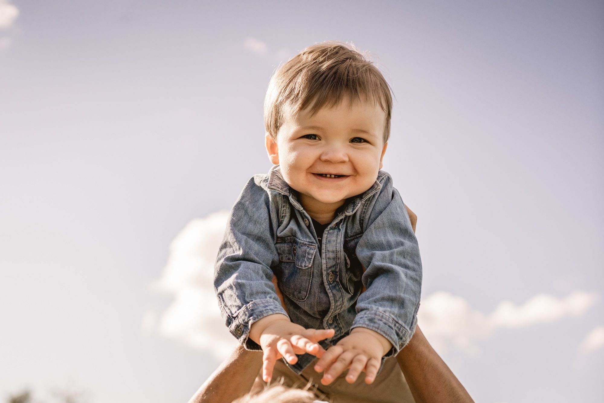 Kind welches frotal zur Kamera hoch in die Luft gehalten wird und dabei lächelt