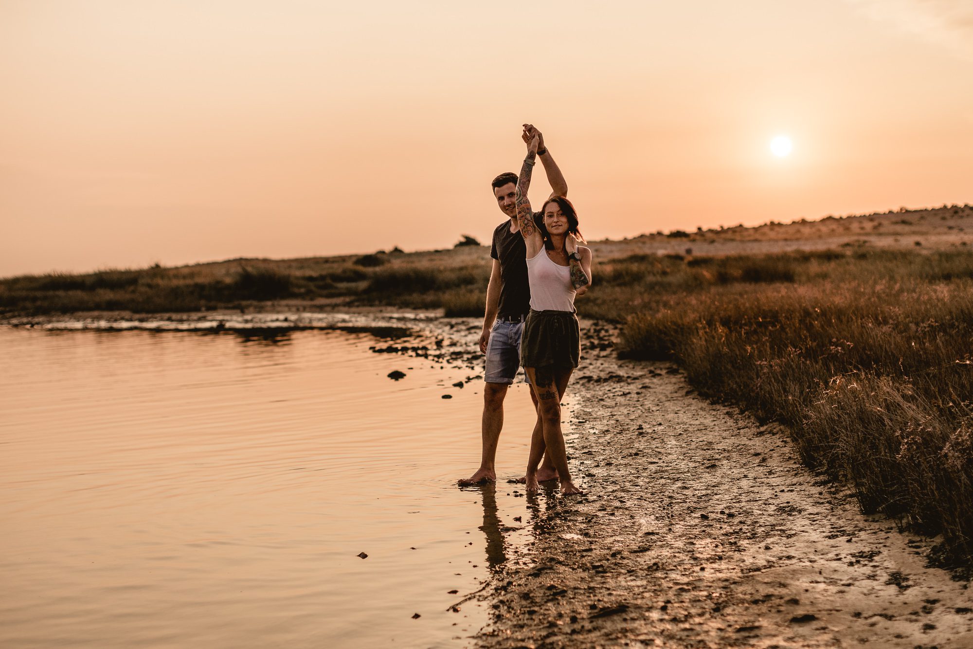 PÄRCHEN tanzend im Sonnenuntergang am kroatischen Meer während eines Pärchenfotoshootings, sie lächeln beide