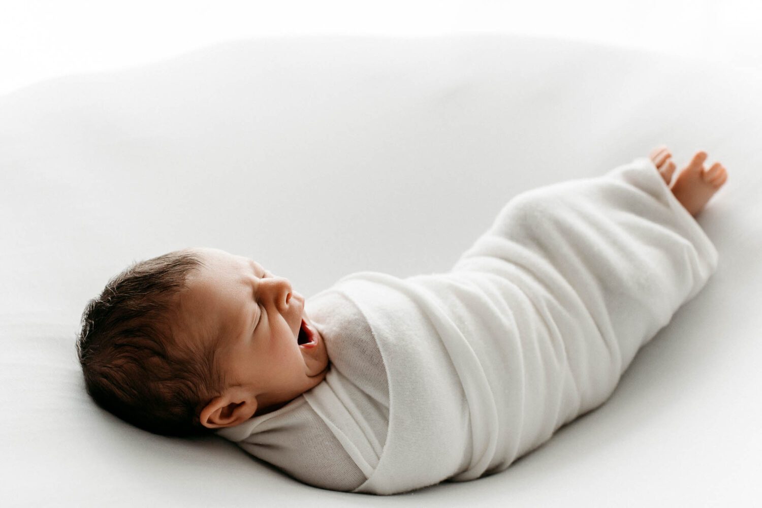 in einem Wrap gehülltes Baby schlafendes Baby, welches gerade gähnt und wach wird