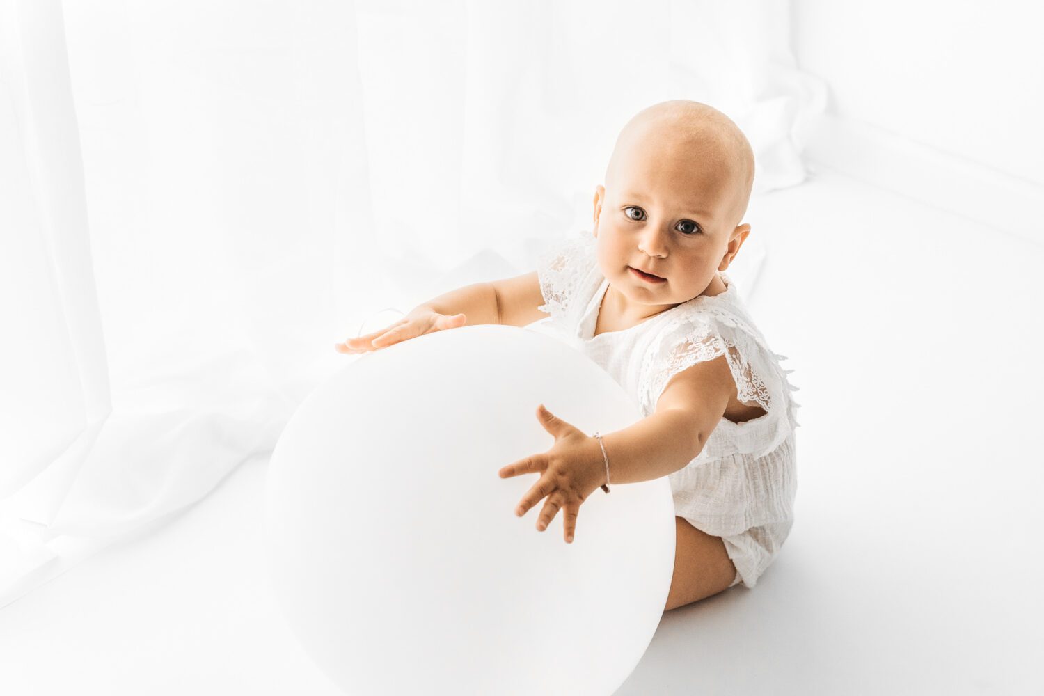 Baby was mit einem großen weißen Luftballon auf dem Boden sitzt