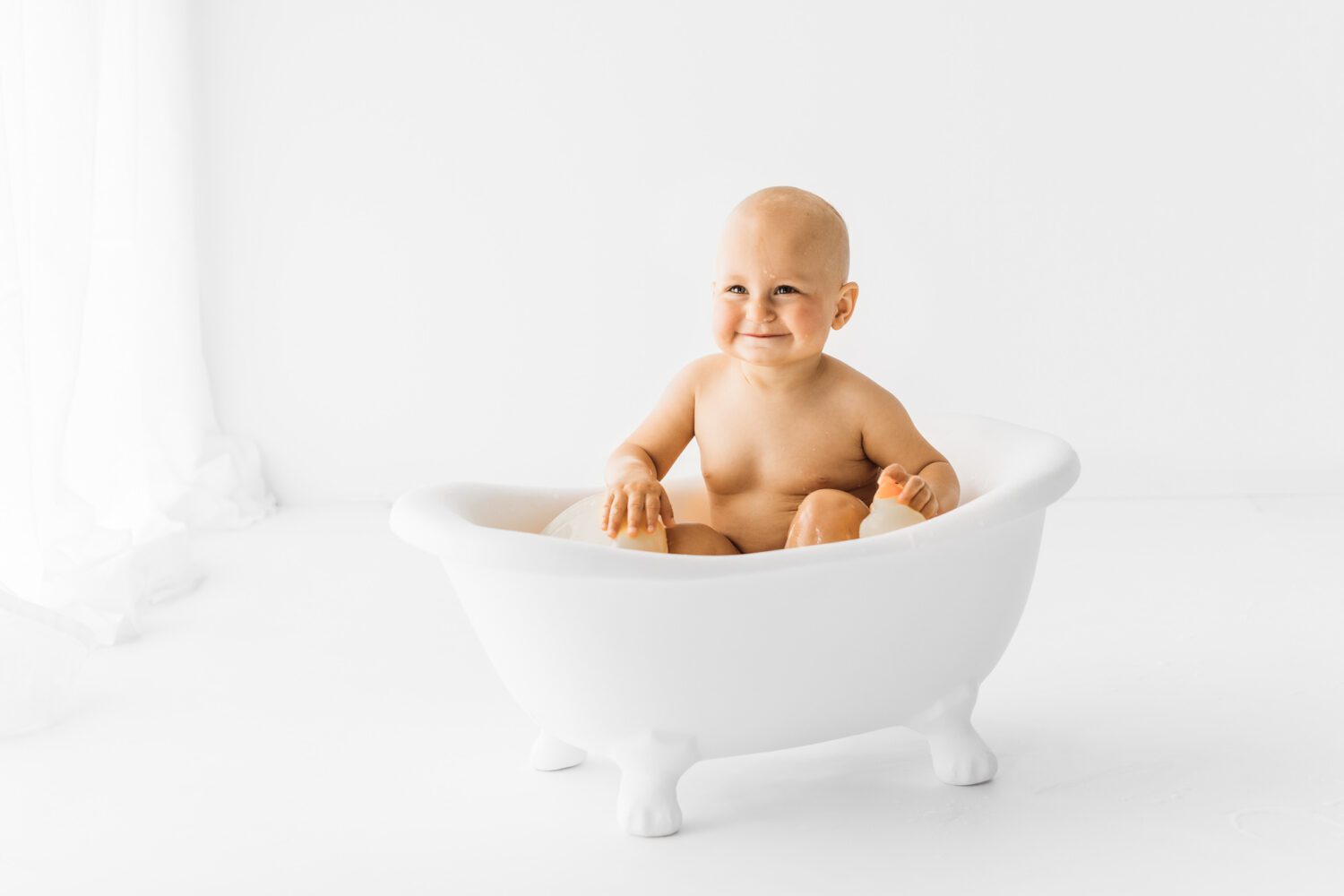 Baby was sehr grinsend in einer kleinen weißen Badewanne sitzt
