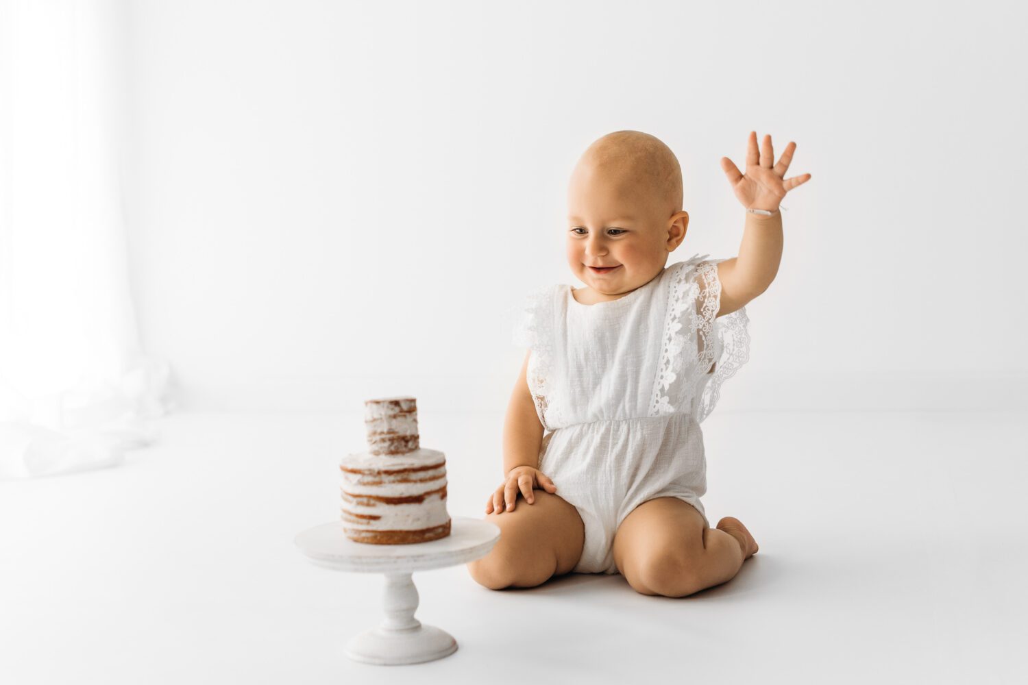 Baby welches vor einem Cake Smash Kuchen sitzt und mit erhobener Hand kurz vor den zermatschen des Kuchen ist