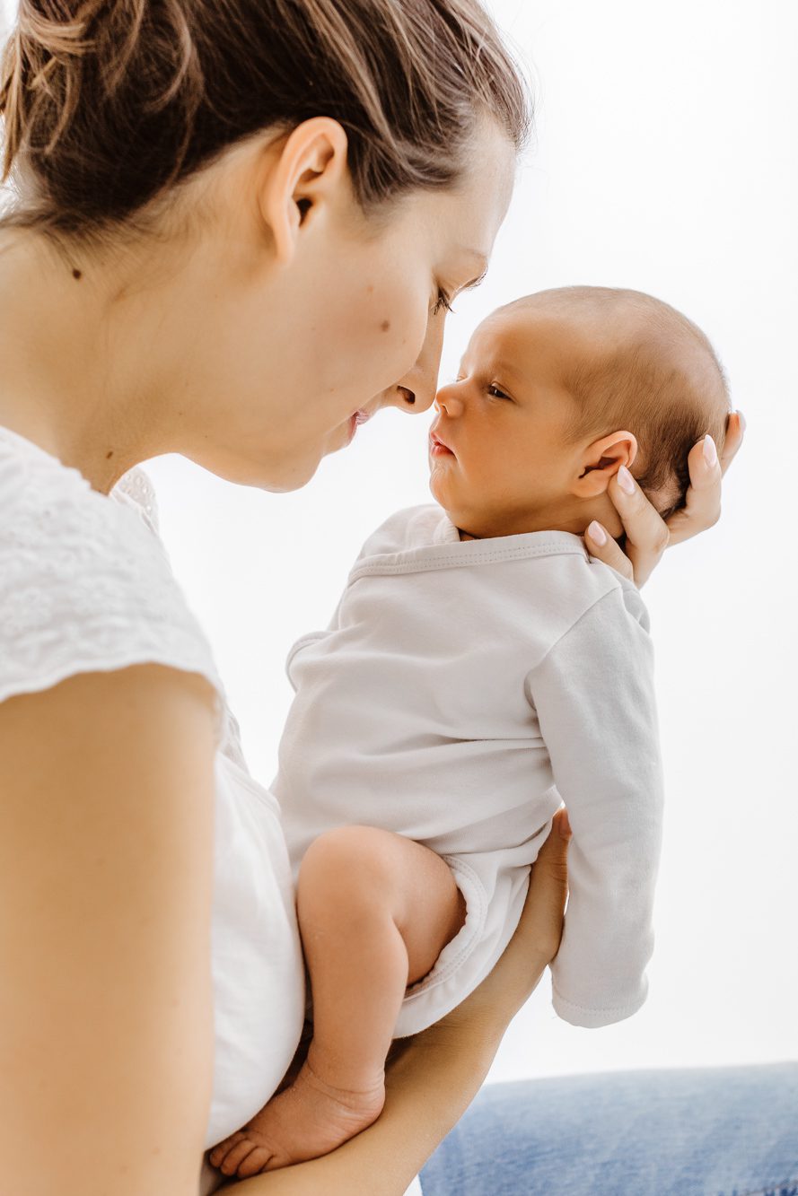 Mutter welches ihr Baby in den Händen hält und es liebevoll im Gesicht kuschelt