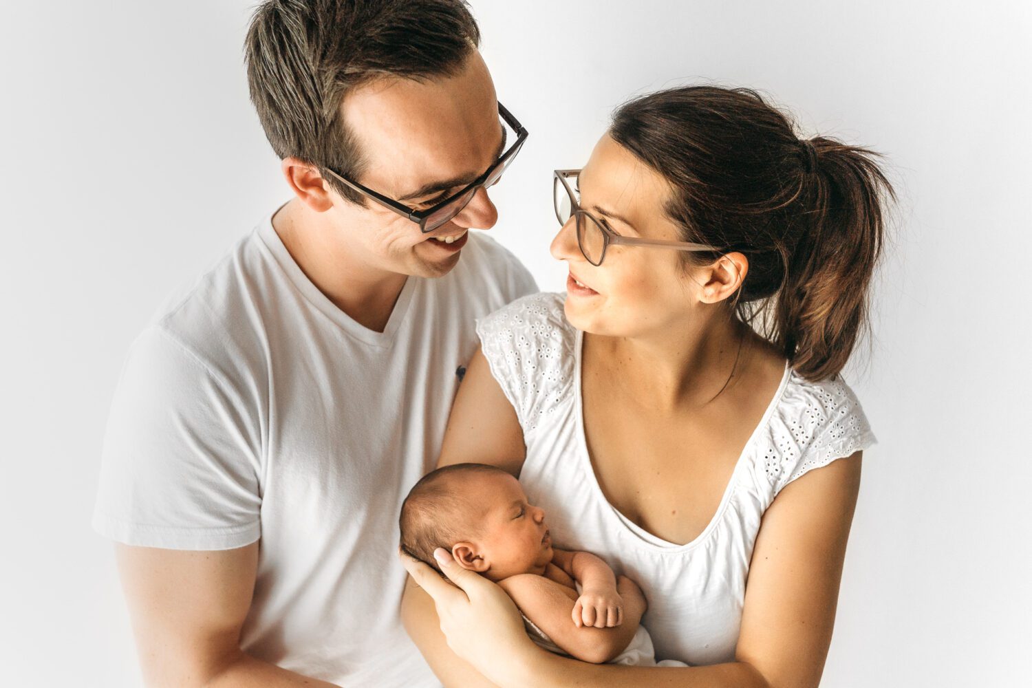 Frisch gebackenen Eltern die sich vor stolz ansehen und lächeln, dabei liegt das Baby bei der Mutter im Arm