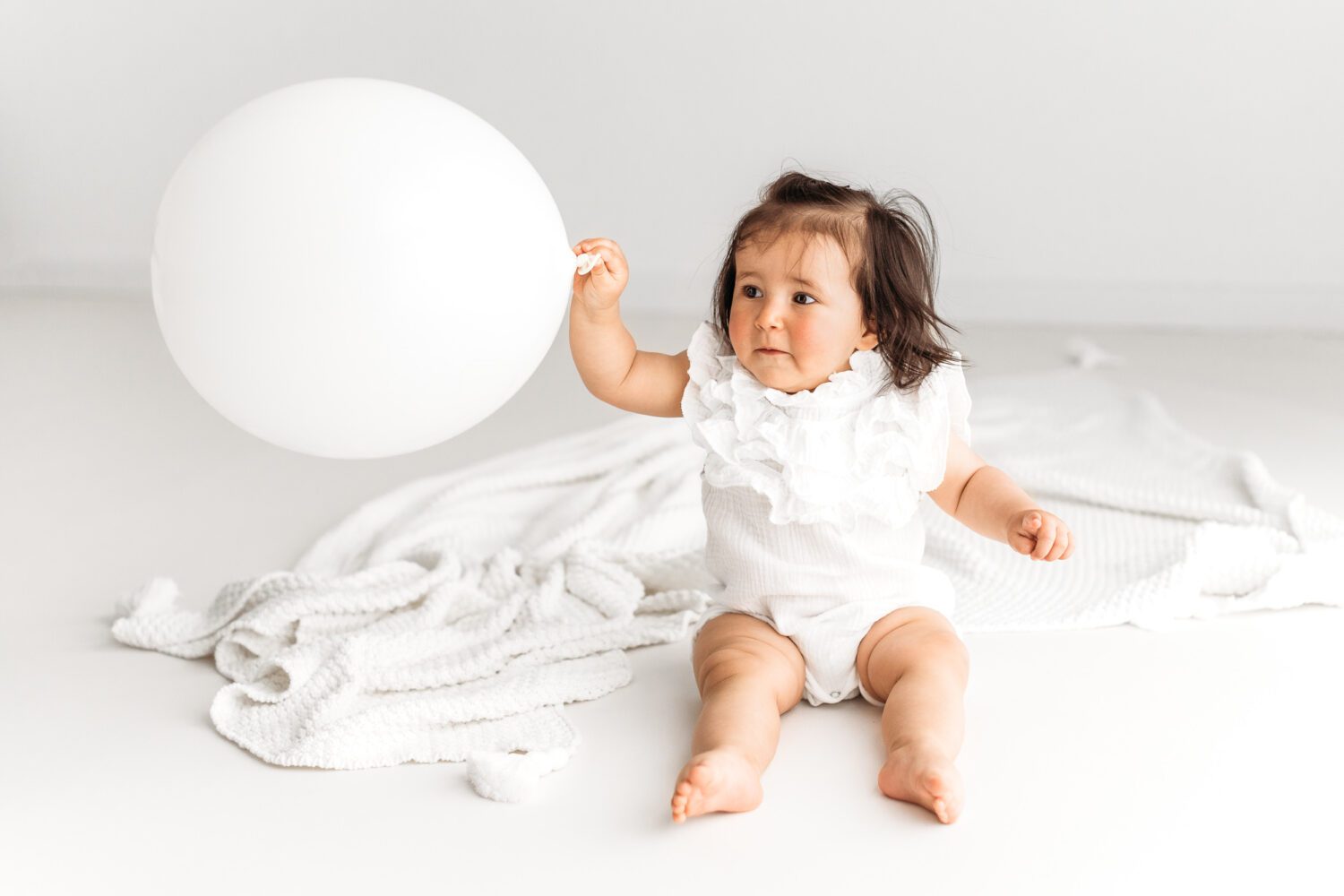 Baby Mädchen in einem Fotostudio fotografiert mit einem weißen Luftballon in der Hand