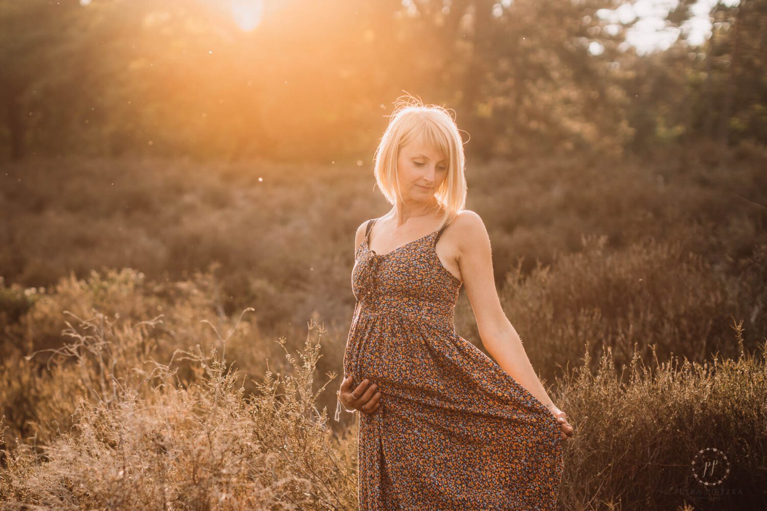 schwangere Frau in einem Kleid dreht sich im schönen Abendlicht und hält ihren babybauch dabei