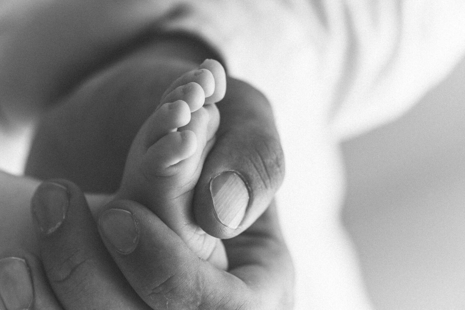 Nahaufnahme schwarz weiß Foto eines Babyfußes gehalten von Papas Hand