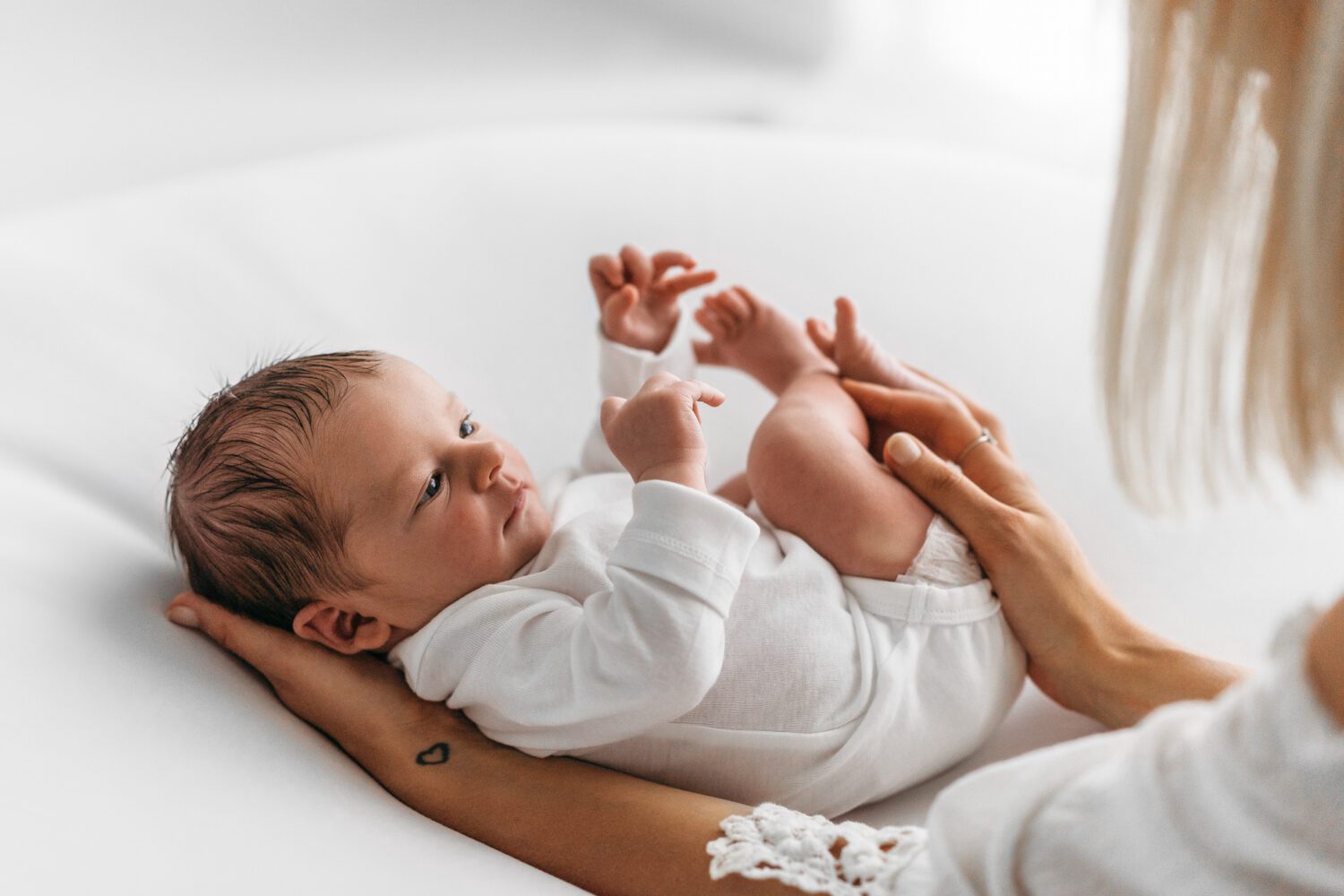 Säugling wie es mit offenen Augen in Richtung seiner Mama schaut, dabei mit dem Kopf in Mams Hand liegt