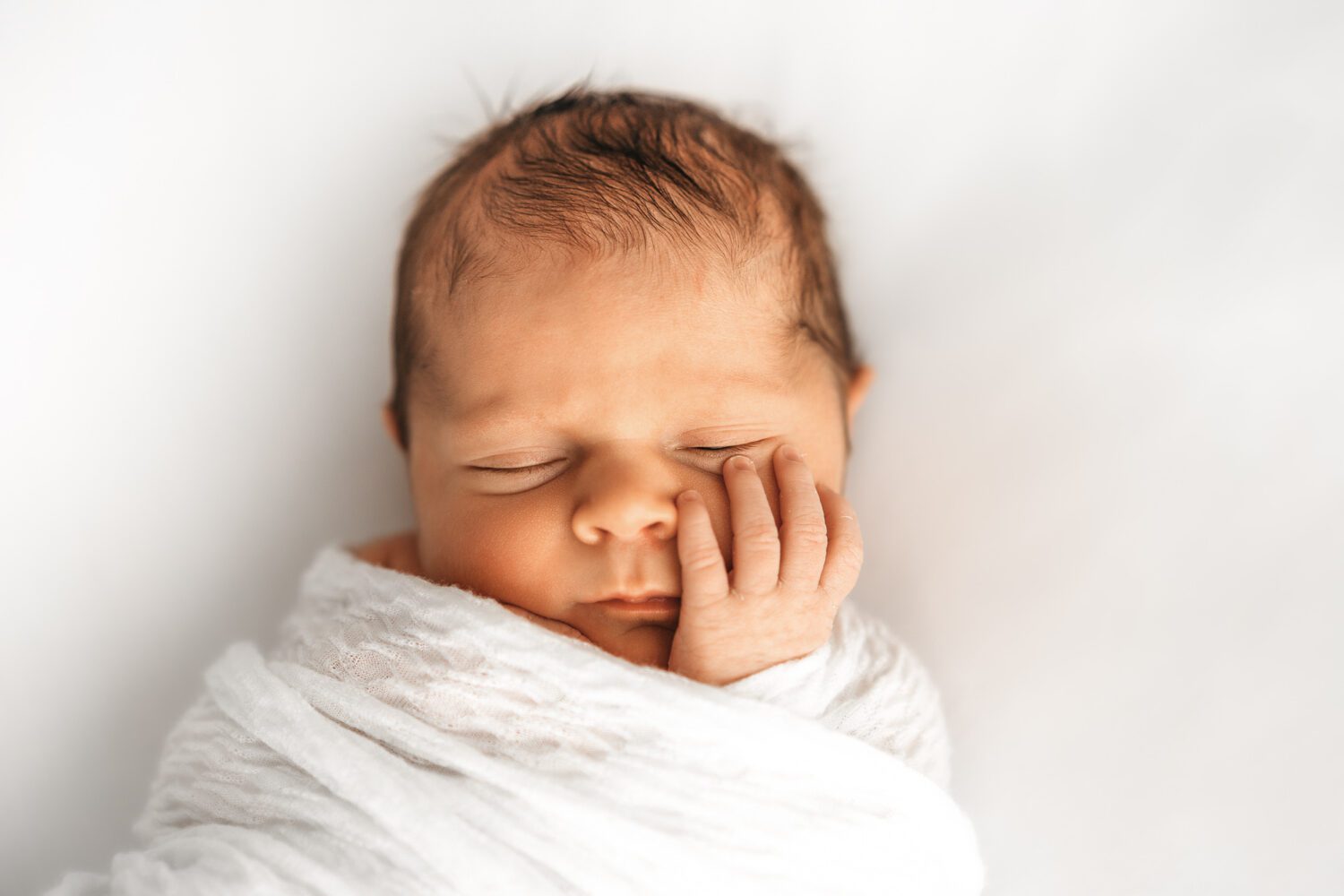 Neugeborenes Baby nah am Kopf fotografiert wie es seine Hand auf der Wange ligen hat und schön eingepuckt schläft