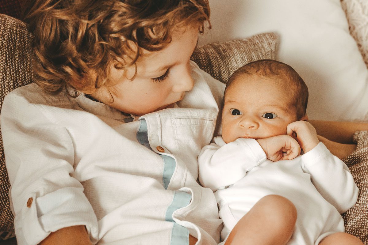 Neugeborenes Baby mit offenen Augen liegt es im Arm des Bruders, wobei dieser seinen kleine Bruder betrachtet