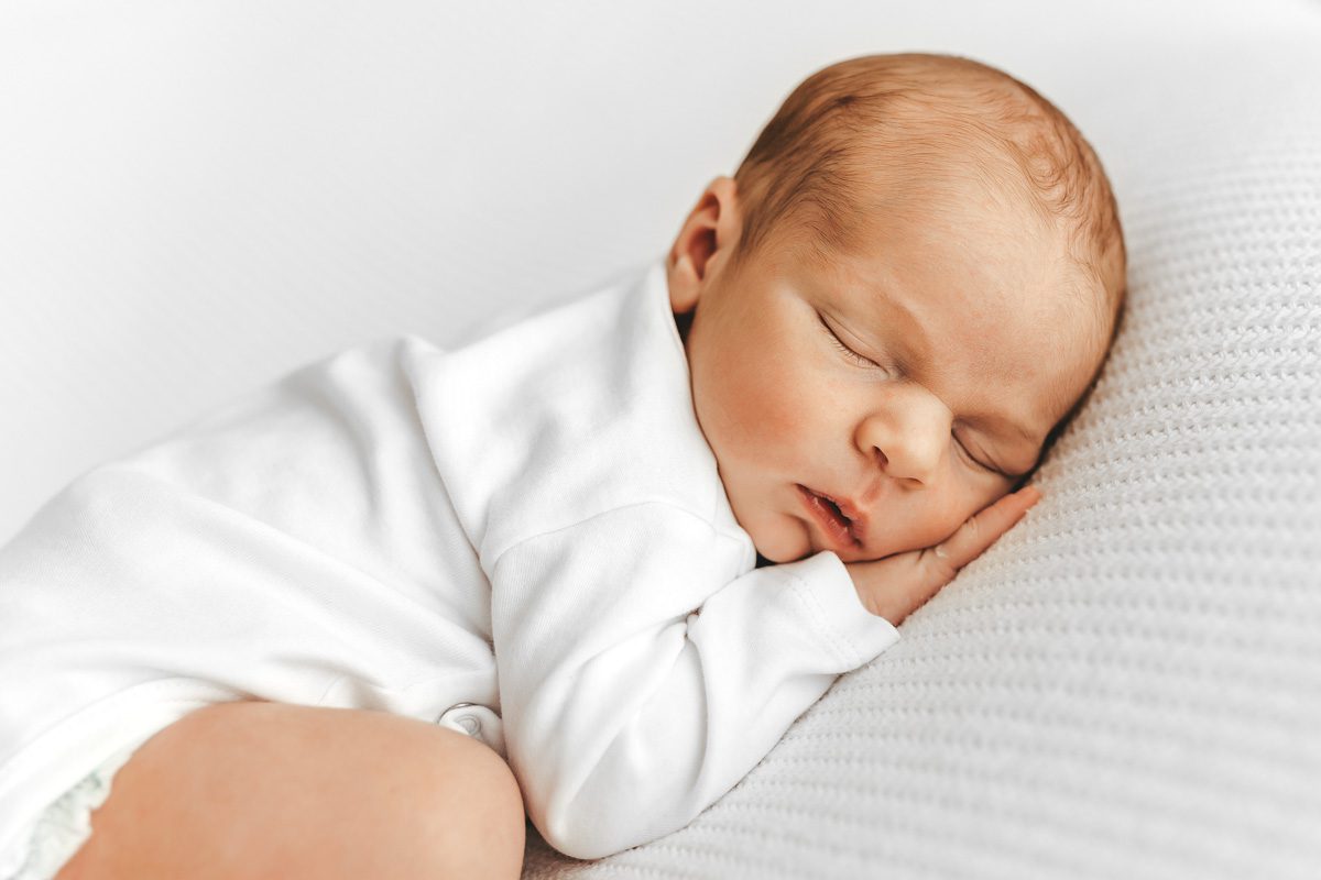 Neugeborenes Baby auf dem Bauch liegend und fest schlafend, dabei hat es eine hand unter dem kopf