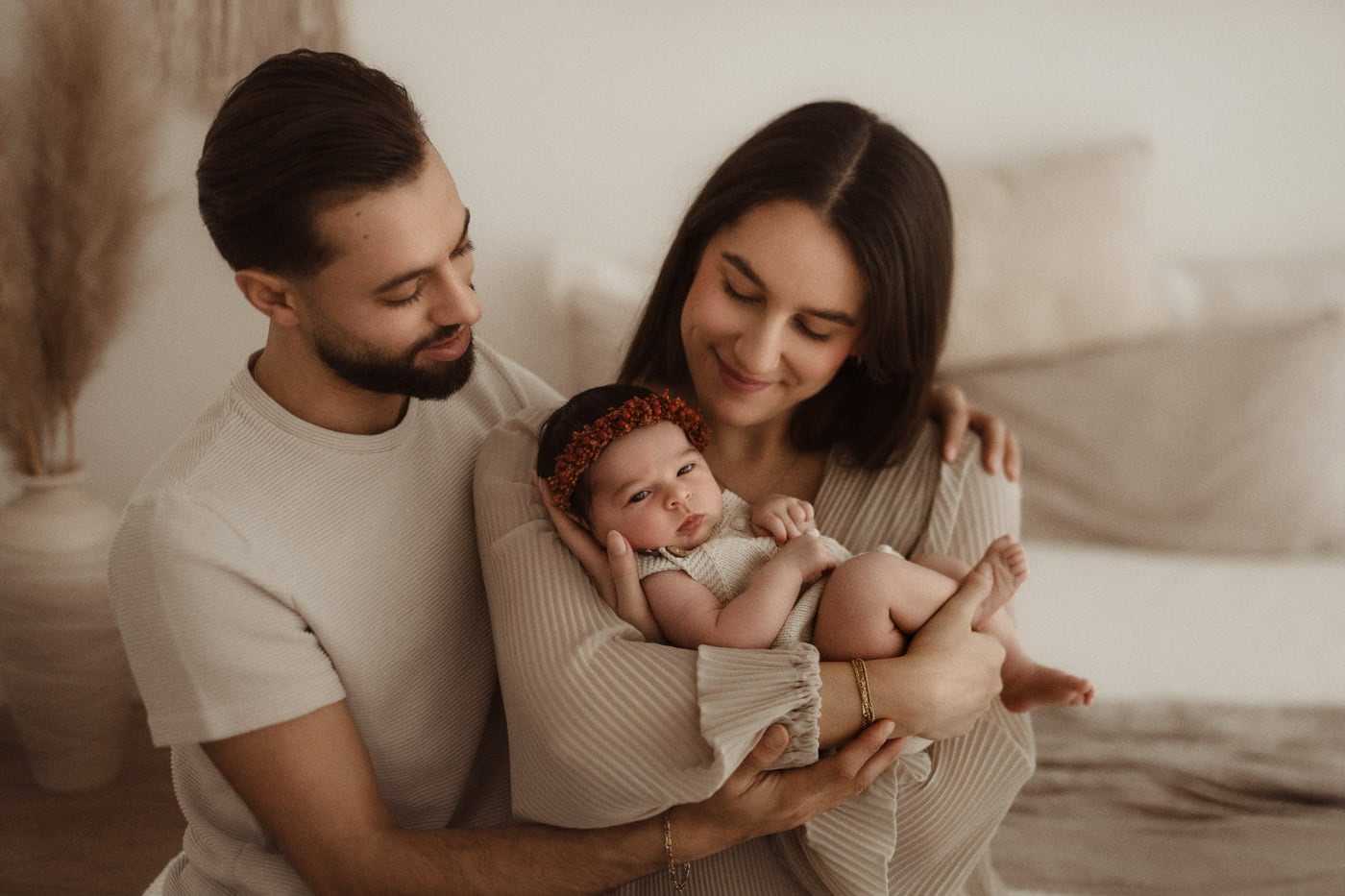 Neugeborenenshooting in Kerpen: Junge Eltern halten ihr waches Baby mit Blumenkranz liebevoll im Arm.